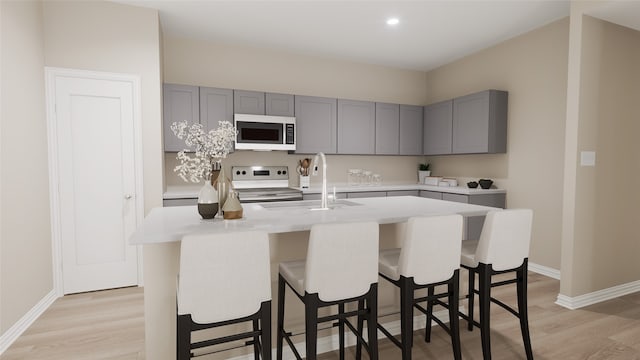 kitchen with range, light wood-type flooring, a kitchen island with sink, light stone countertops, and sink