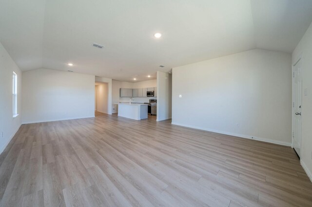 unfurnished living room with sink, vaulted ceiling, and light hardwood / wood-style flooring