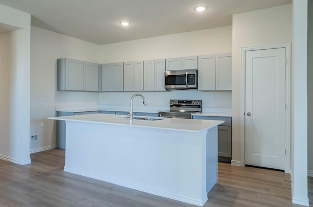 kitchen featuring sink, a center island with sink, gray cabinets, stainless steel appliances, and light hardwood / wood-style floors