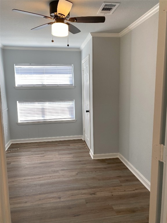 unfurnished room with baseboards, visible vents, a ceiling fan, dark wood-style floors, and crown molding