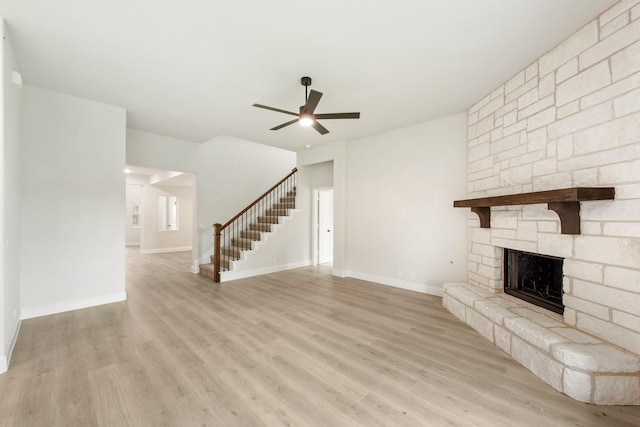 unfurnished living room featuring a stone fireplace, ceiling fan, and light wood-type flooring