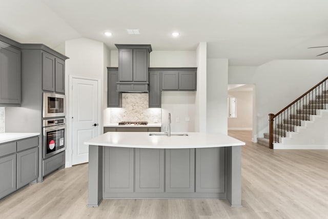 kitchen with gray cabinetry, sink, ceiling fan, light hardwood / wood-style floors, and stainless steel appliances