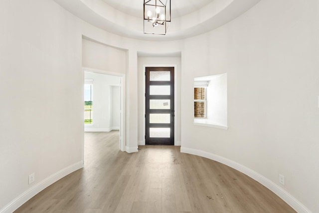 entryway featuring light hardwood / wood-style flooring, a raised ceiling, and a notable chandelier