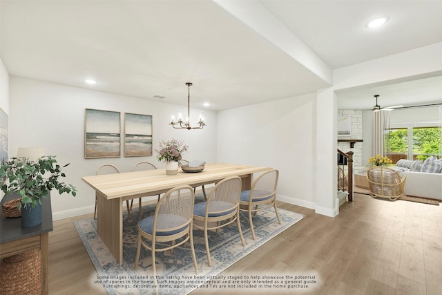 dining space with a stone fireplace, ceiling fan with notable chandelier, and light wood-type flooring