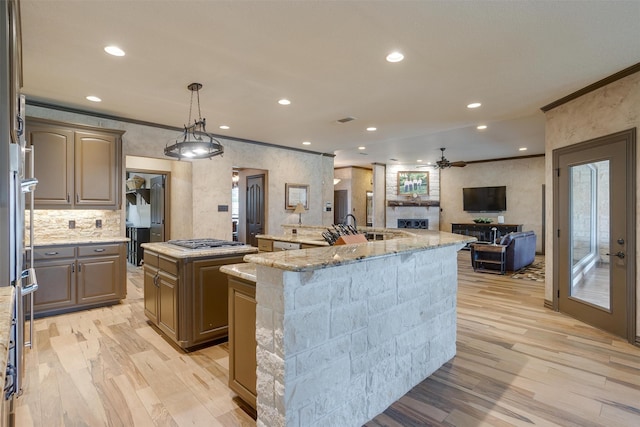 kitchen featuring ceiling fan, ornamental molding, light hardwood / wood-style flooring, and a center island with sink