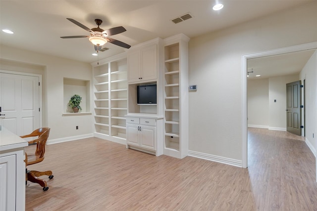 unfurnished office with built in shelves, ceiling fan, and light wood-type flooring