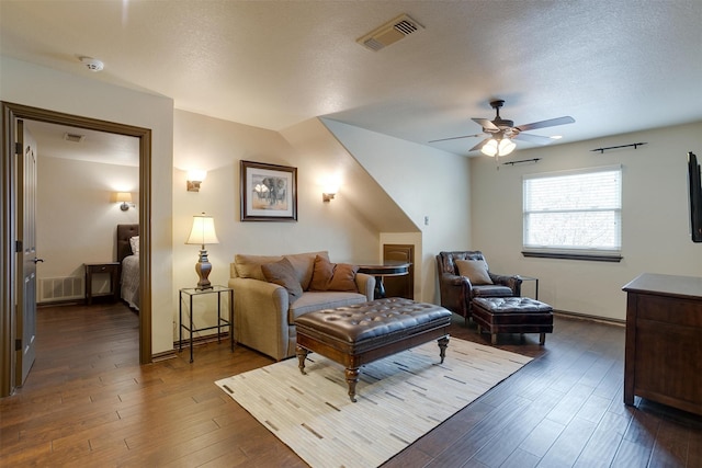 living room with a textured ceiling, ceiling fan, and dark wood-type flooring