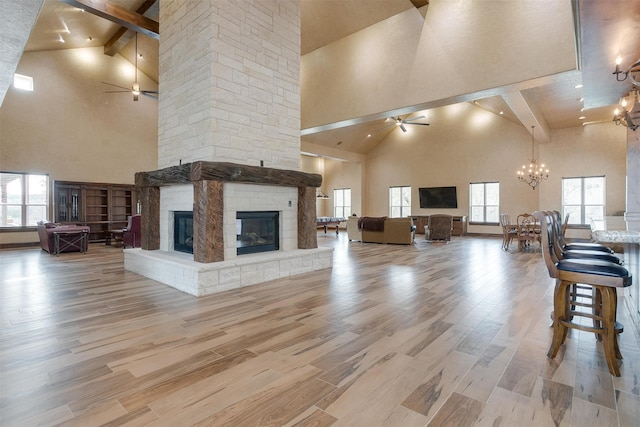 unfurnished living room featuring a fireplace, wood-type flooring, ceiling fan with notable chandelier, high vaulted ceiling, and beamed ceiling