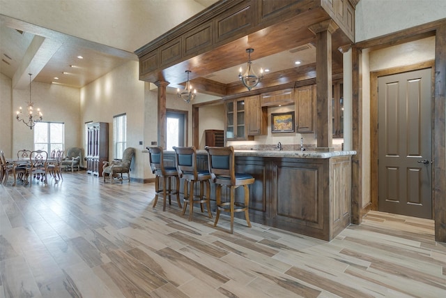 kitchen featuring an inviting chandelier, pendant lighting, kitchen peninsula, a kitchen breakfast bar, and a towering ceiling