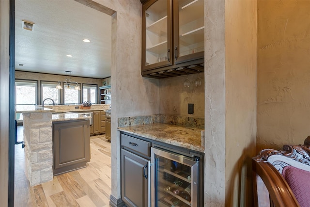 bar with beverage cooler, light stone counters, light wood-type flooring, and pendant lighting