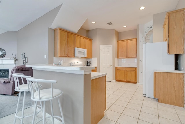 kitchen featuring light brown cabinets, light tile patterned floors, kitchen peninsula, white appliances, and a fireplace