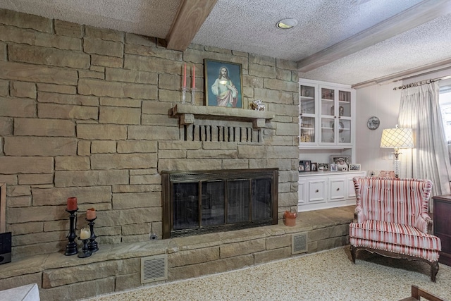 carpeted living room with a textured ceiling, a stone fireplace, and beamed ceiling