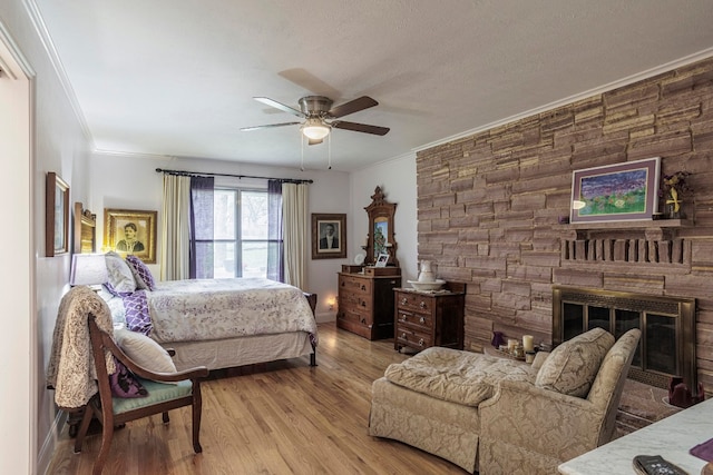 bedroom featuring a stone fireplace, light hardwood / wood-style floors, ceiling fan, and crown molding