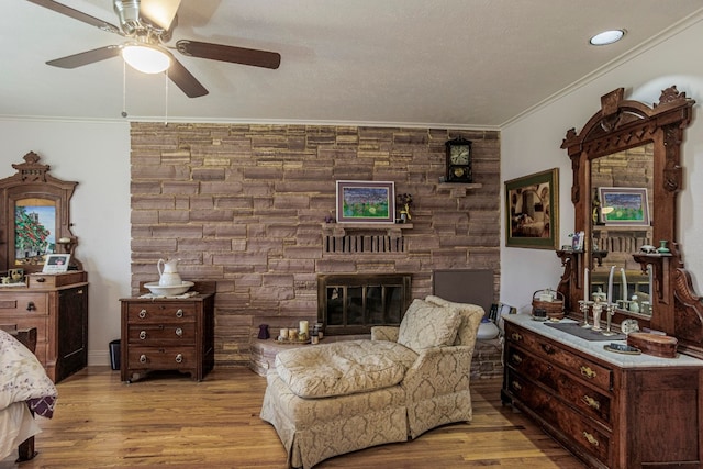 living room featuring ornamental molding, light hardwood / wood-style floors, ceiling fan, and a fireplace