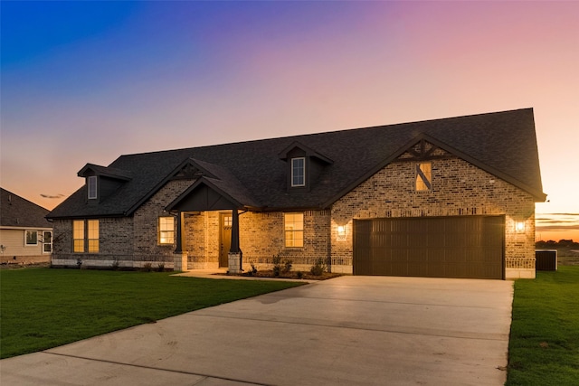 view of front of house with a yard, roof with shingles, concrete driveway, an attached garage, and brick siding