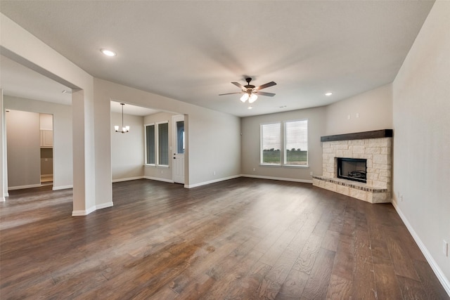 unfurnished living room featuring dark wood-style floors, a stone fireplace, ceiling fan with notable chandelier, and baseboards