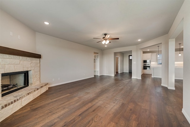 unfurnished living room with baseboards, a fireplace, dark wood-style flooring, and a ceiling fan