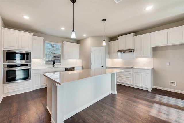 kitchen featuring dark wood finished floors, a sink, white cabinets, under cabinet range hood, and appliances with stainless steel finishes