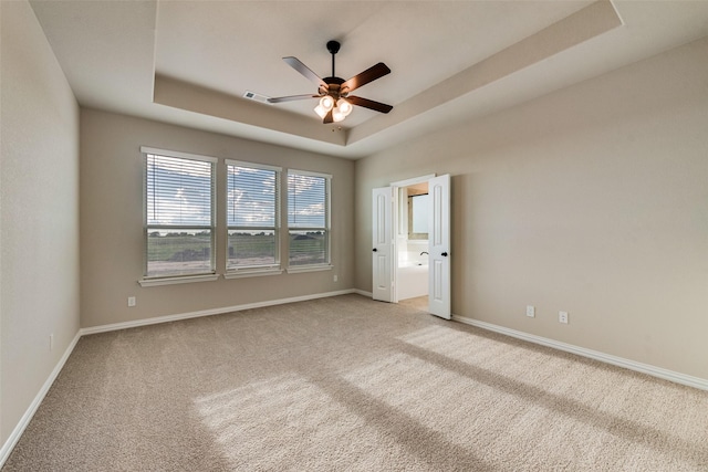 unfurnished room with visible vents, baseboards, a tray ceiling, light carpet, and a ceiling fan