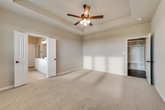 unfurnished bedroom with a tray ceiling, a spacious closet, light colored carpet, and baseboards