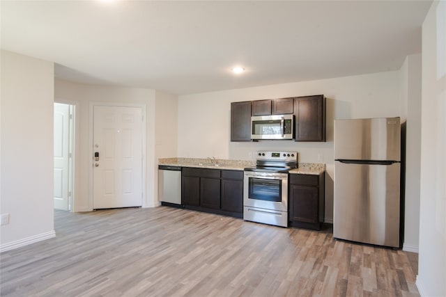 kitchen with light stone countertops, appliances with stainless steel finishes, dark brown cabinetry, light wood-type flooring, and sink