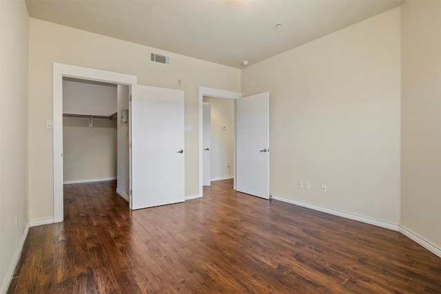 unfurnished bedroom featuring a closet, a spacious closet, and dark hardwood / wood-style flooring