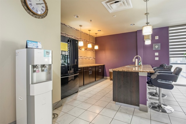 kitchen featuring black refrigerator with ice dispenser, decorative light fixtures, sink, light tile floors, and dark brown cabinets