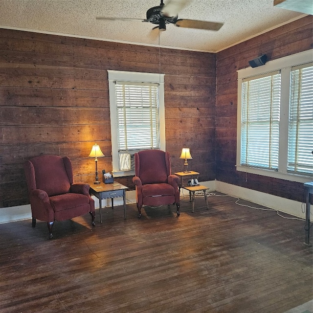 sitting room with wood walls, ceiling fan, dark hardwood / wood-style floors, and a wealth of natural light