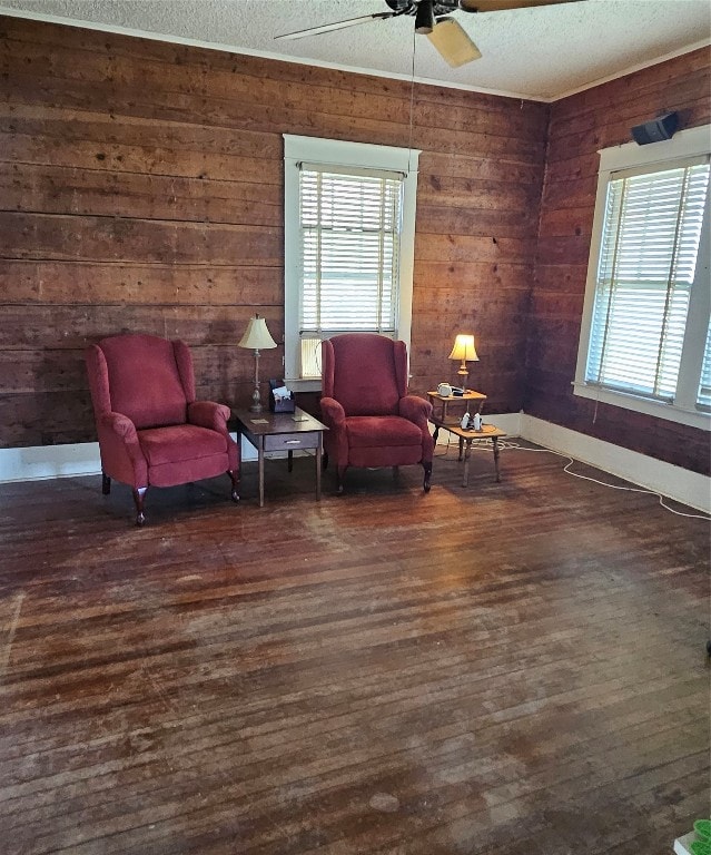 sitting room with ceiling fan, dark hardwood / wood-style floors, wood walls, and a textured ceiling