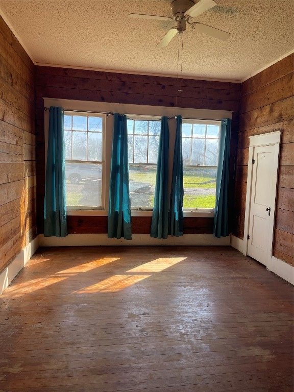 empty room featuring ceiling fan, dark wood-type flooring, wood walls, and a textured ceiling