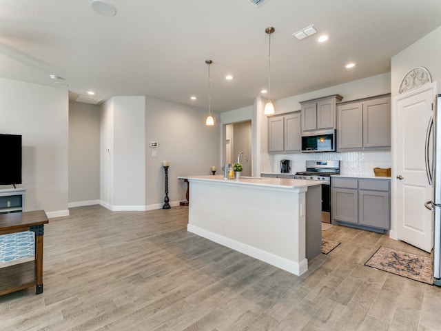 kitchen featuring backsplash, stainless steel appliances, decorative light fixtures, gray cabinets, and an island with sink