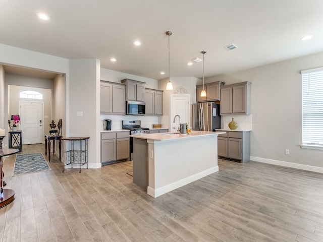 kitchen with light hardwood / wood-style floors, stainless steel appliances, sink, a center island with sink, and gray cabinets