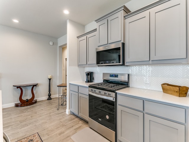 kitchen with backsplash, gray cabinetry, light wood-type flooring, and appliances with stainless steel finishes