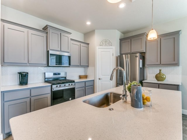 kitchen featuring gray cabinetry, a sink, appliances with stainless steel finishes, decorative backsplash, and decorative light fixtures