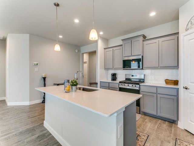 kitchen featuring gray cabinetry, sink, an island with sink, appliances with stainless steel finishes, and decorative light fixtures