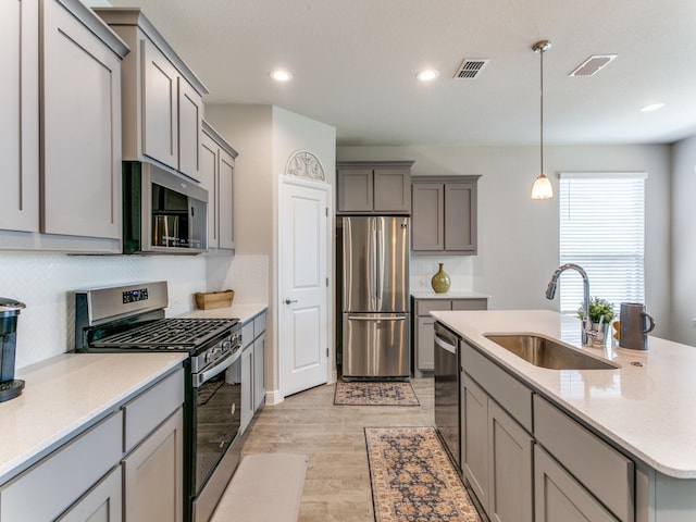 kitchen with appliances with stainless steel finishes, backsplash, sink, pendant lighting, and gray cabinets