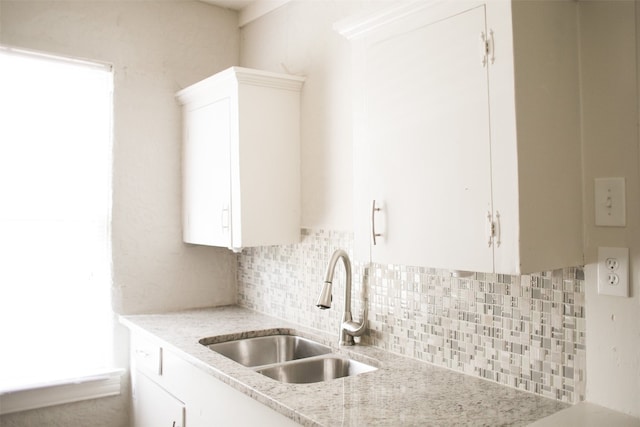 kitchen featuring sink, tasteful backsplash, light stone counters, and white cabinets