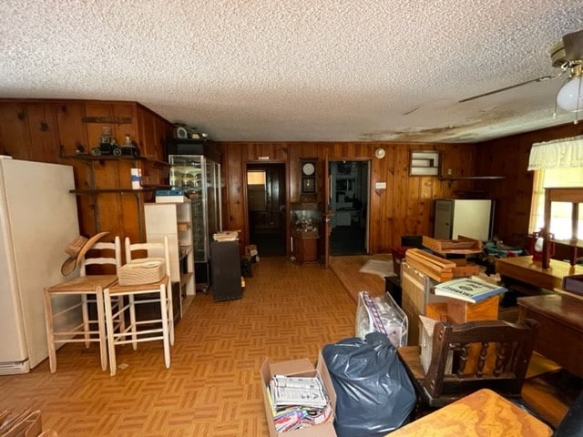 interior space featuring light parquet floors, wood walls, ceiling fan, and a textured ceiling