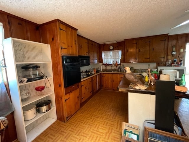 kitchen with light parquet floors, a textured ceiling, and black appliances