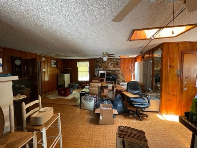 living room with wooden walls, ceiling fan, light parquet floors, a textured ceiling, and a stone fireplace