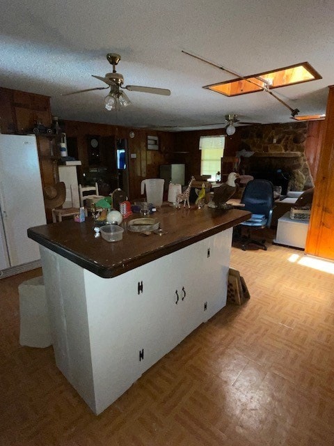 kitchen with a textured ceiling, ceiling fan, light parquet floors, and a stone fireplace