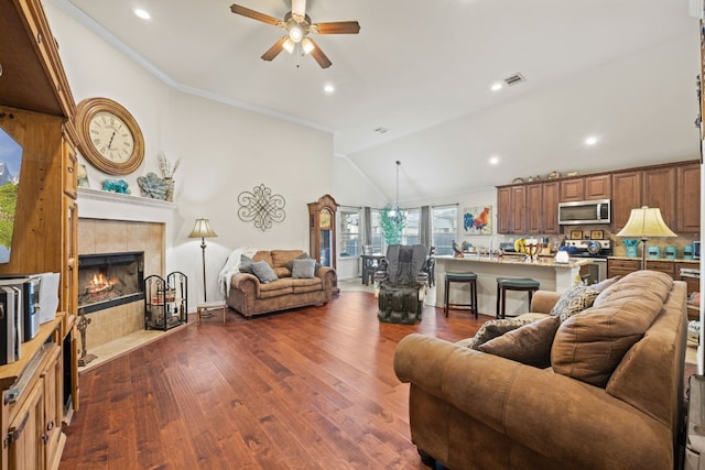 living room with ceiling fan, crown molding, a tiled fireplace, dark wood-type flooring, and high vaulted ceiling