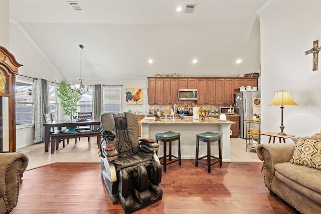 living room with high vaulted ceiling, sink, light wood-type flooring, a chandelier, and ornamental molding