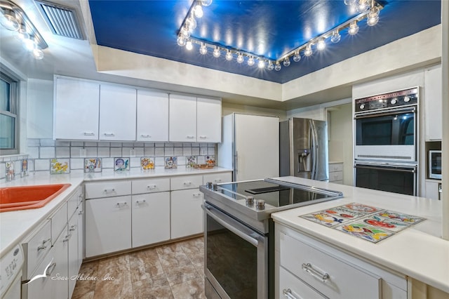 kitchen featuring appliances with stainless steel finishes, backsplash, light tile flooring, a tray ceiling, and white cabinetry