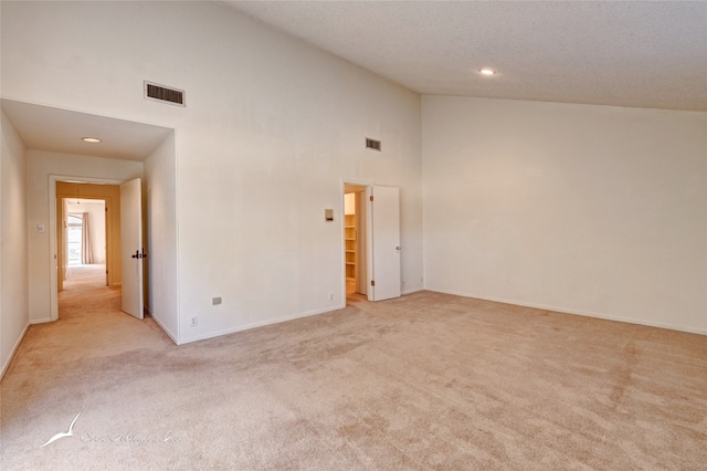 empty room with light carpet, high vaulted ceiling, and a textured ceiling