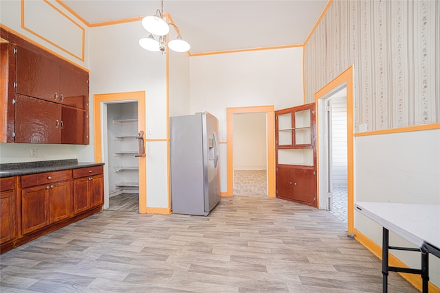 kitchen featuring stainless steel fridge, decorative light fixtures, light hardwood / wood-style flooring, ornamental molding, and a high ceiling