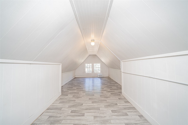 additional living space with light wood-type flooring, lofted ceiling, and wood walls