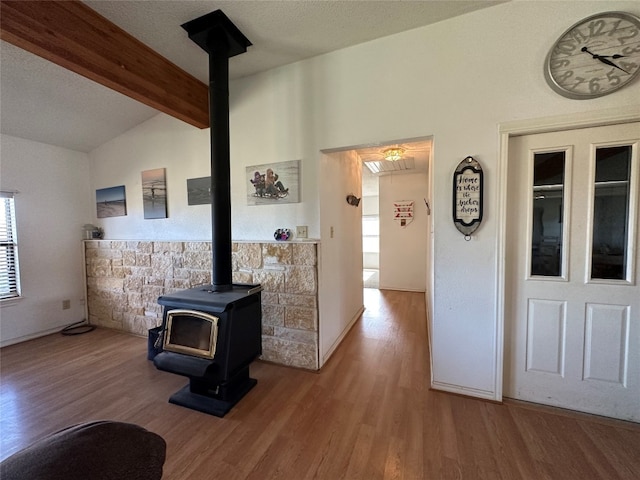 living room featuring lofted ceiling with beams, plenty of natural light, wood-type flooring, and a wood stove