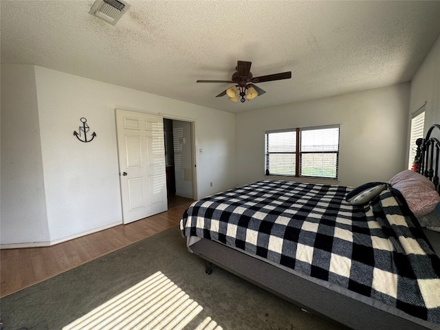 bedroom with a textured ceiling, ceiling fan, and dark wood-type flooring