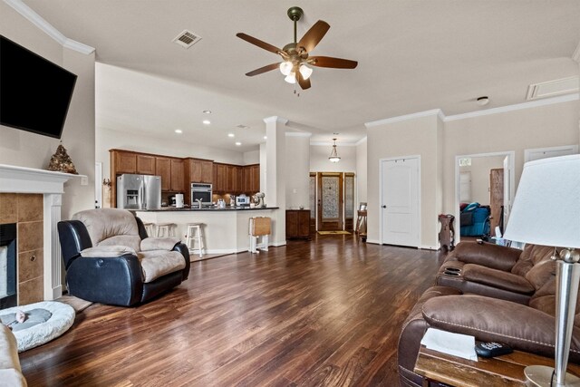 living room with ceiling fan, dark wood-type flooring, ornamental molding, and a tiled fireplace